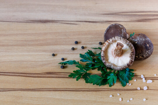 Fresh shiitake mushrooms with green parsley, black peppercorns and coarse salt on wooden table with copy space, gourmet cooking concept