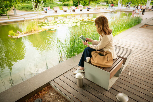 Rear view of a woman sitting in a city park and using a digital tablet