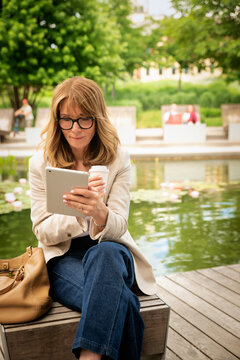 Confident mid-aged woman sitting in a city park and using a digital tablet