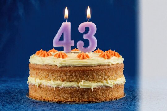 Layered birthday cake with cream frosting and orange dots features purple numeral candles showing forty three. A celebratory confection waits for a wish.