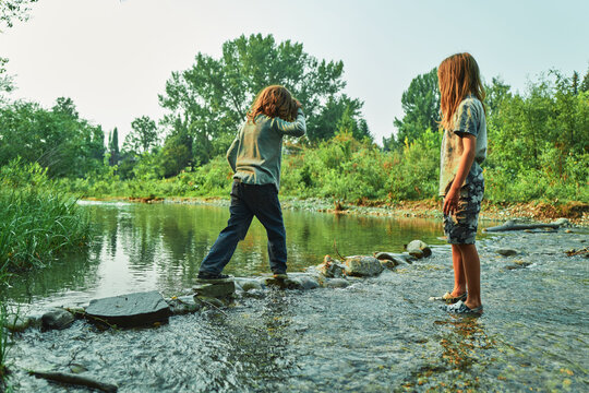 Two boys crossing a shallow river on stepping stones