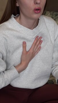 Young woman holding her chest while breathing heavily and experiencing shortness of breath and discomfort at home.