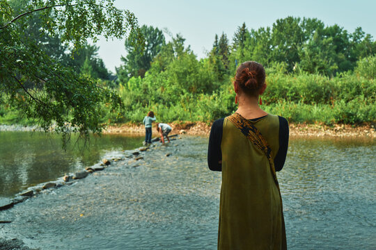 Woman watching children play at a river from behind