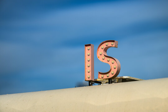 Vintage rooftop sign with large illuminated letters against sky.