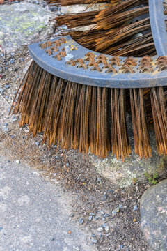 Rusty circular street sweeper brush resting on ground.