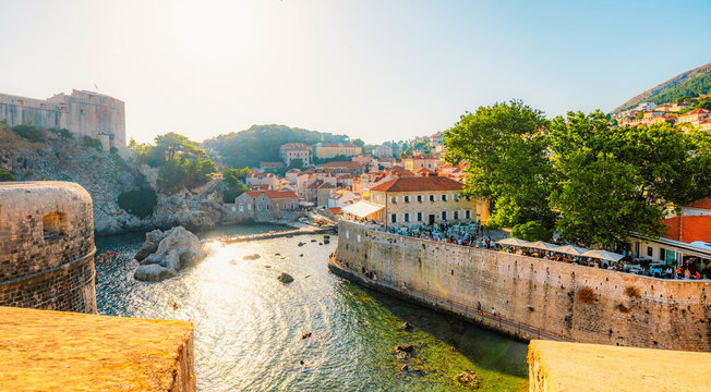 Golden hour panorama of Dubrovnik's historic fortifications and old port at dusk, featuring sunlight on ancient stone walls and Mediterranean architecture in Croatia