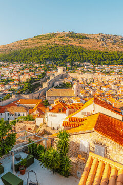 Golden hour panorama of Dubrovnik's historic fortifications and old port at dusk, featuring sunlight on ancient stone walls and Mediterranean architecture in Croatia