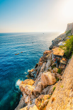 Golden hour panorama of Dubrovnik's historic fortifications and old port at dusk, featuring sunlight on ancient stone walls and Mediterranean architecture in Croatia