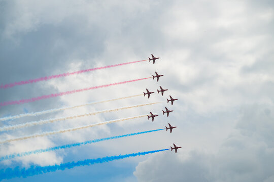 Aerobatic team flying straight smoke trails across dramatic cloudy sky.
