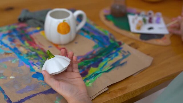 Female child painting on a pumpking cup during fall season for Halloween event - Holiday, childhood and autumn lifestyle concept	