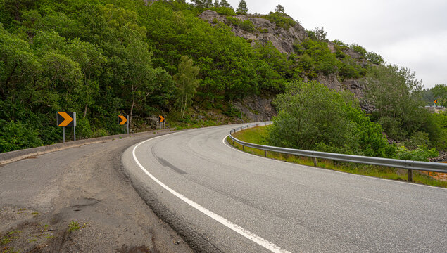 Curving mountain road with guardrails surrounded by dense green forest.
