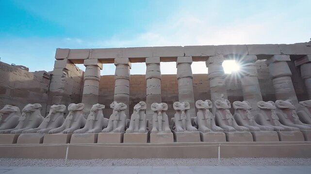 Ram-headed sphinx statues avenue in Karnak Temple with sun shine in background, Luxor. Antique luxor monuments from sandstone. cultural heritage of Egypt. 