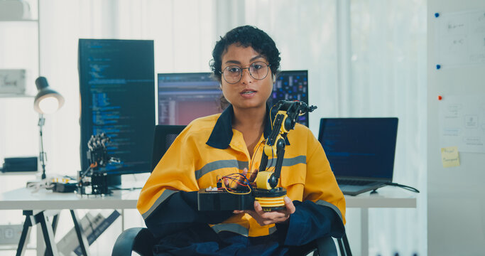Young African American female robotics engineer discussing mechanical part on video call and looking at camera in laboratory. Remote work, virtual training, online meeting, future technology concept.