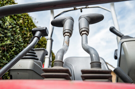 Abstract view of the control levers for the scoop and driving tracks of a small mechanical digger seen parked in a private drive before exaction.  The middle levers control the hydraulic scoop arm.