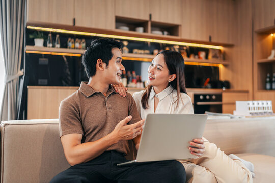 Young adult couple financial partners discussing future real estate investment plans together using laptop computer modern home living room apartment