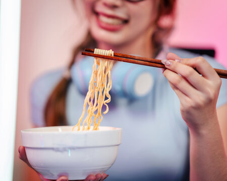Enthusiastic content creator streamer gamer enjoys delicious instant noodles with chopsticks from a white bowl during a relaxing long session