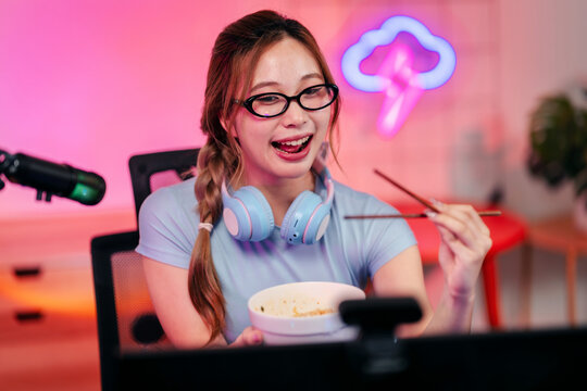 Happy female streamer eats quick meal during live broadcast in vibrant home gaming studio environment