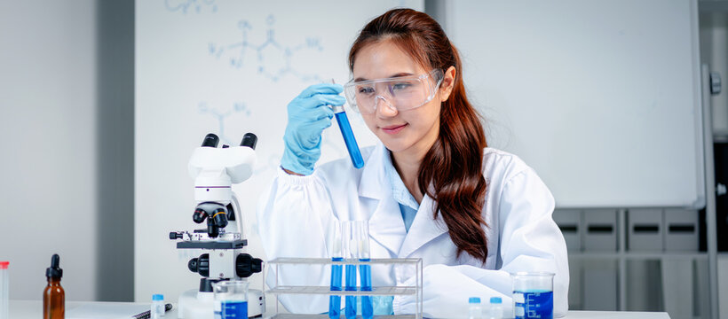 Female scientist conducts chemical experiment examining blue liquid test tube professional laboratory research development analytical work