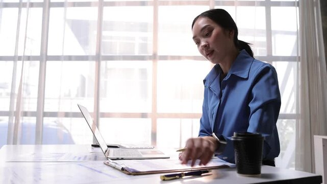 Professional Asian businesswoman discussing business strategy and presenting financial data charts to colleagues during an online video meeting.
