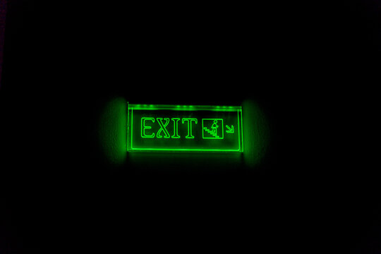 Glowing green exit sign with directional arrow on black background, symbolizing emergency escape and safety in public or commercial spaces.