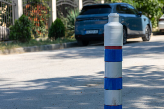Plastic traffic bollard with blue reflective bands on a sunny city street, parked car and greenery in the background, emphasizing urban safety.