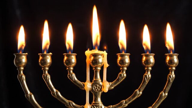 Lit golden brass menorah with seven flames on black background