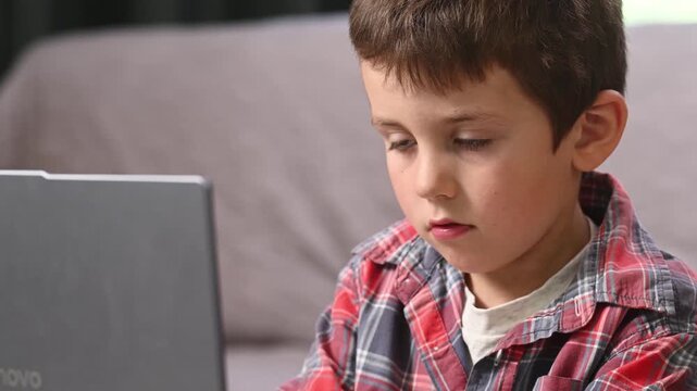 School age boy reviews online educational materials on laptop before completing written homework in notebook, highlighting effective study habits and educational technology 