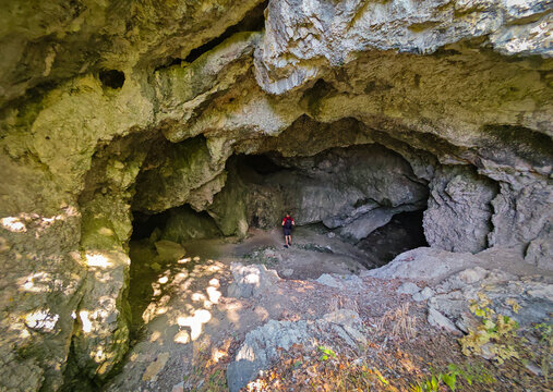 Hiker exploring the large rocky entrance chamber of H&aacute;rom-k&uacute;ti Cave in the B&uuml;kk Mountains, Hungary, surrounded by impressive limestone formations.