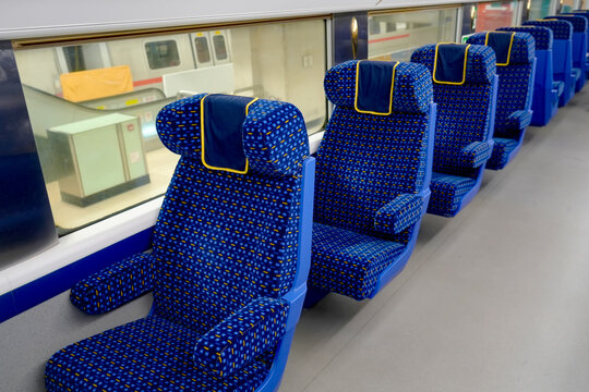 Rows of blue patterned chairs sit inside a quiet train car while natural daylight shines through the clear windows on a calm afternoon