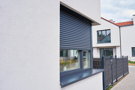 Partially lowered roller shutter covers window on modern house beside fenced residential street