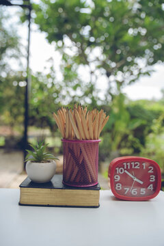 Desk for student education concept. Book, clock, and pencil holder for study for exam placed on wooden School table with garden background for student plan to work at home-vertical image.