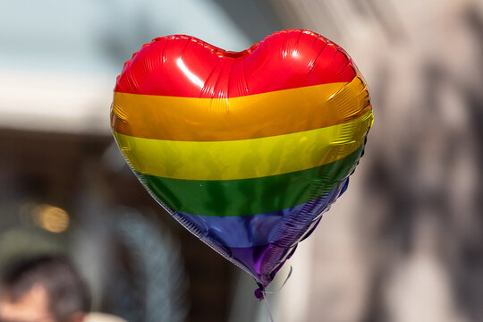 Ein herzf&ouml;rmiger Luftballon in Regenbogenfarben schwebt &uuml;ber der N&uuml;rnberger Innenstadt w&auml;hrend des Christopher Street Day. Im unscharfen Hintergrund sind Teilnehmer der Parade zu erkennen.