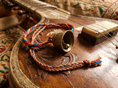 Musical themed braided thread rakhi with a small brass bell on a sitar