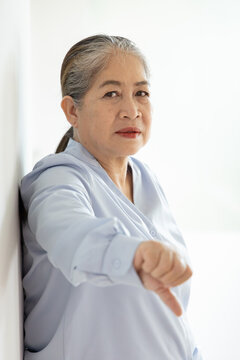 Unhappy and upset old woman with white or silver hair showing rejecting, disapproving, turning down thumb down hand gesture