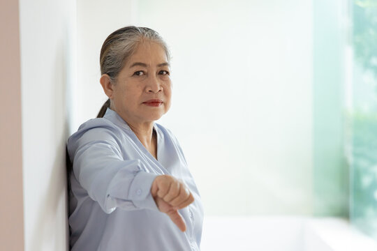 Unhappy and upset old woman with white or silver hair showing rejecting, disapproving, turning down thumb down hand gesture