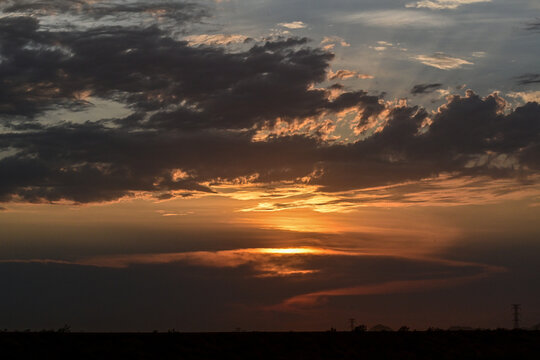 Sunset over a desert landscape with dramatic clouds silhouetted against the horizon, illustrating atmospheric conditions, natural scenery, and evening light