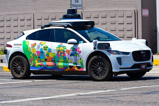 Waymo autonomous Jaguar electric taxi with colorful promotional wrap parked on an urban street, illustrating self-driving technology, electric mobility, and autonomous transportatio