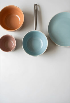 Assortment of pastel colored ceramic kitchenware including bowls, a saucepan, and a plate on a white background