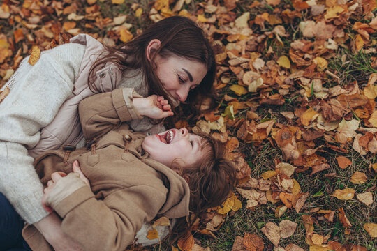 Mother and child laughing while playing in autumn leaves. Joyful, authentic moment of maternal love and family bonding, happiness, family lifestyle, outdoor activities.