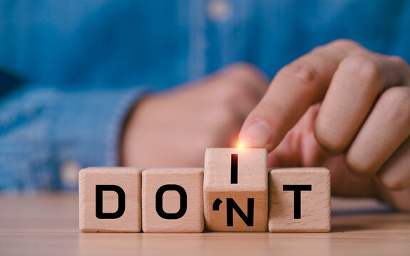 Hand turning a wooden letter block to change DON'T into DO IT symbolizing decision making, growth mindset motivation, challenge choice with personal attitude and business strategy concept.