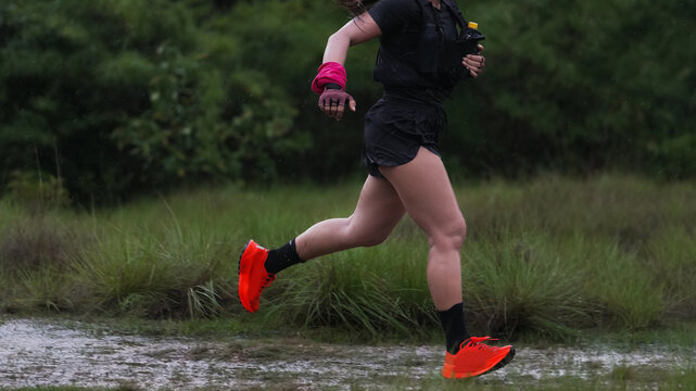 Female trail runner wearing bright red running shoes on a wet forest trail