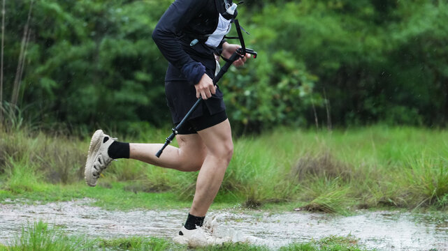 Trail runner using trekking poles while running through a wet forest trail in the rain