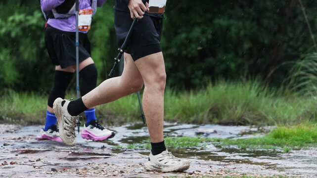 Trail runners crossing a wet forest trail with trekking poles during an outdoor endurance race