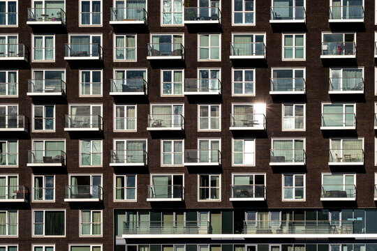 Across London, Isle of Dogs, England, a brick facade of residential apartments sets windows and balconies into a disciplined pattern with late light.