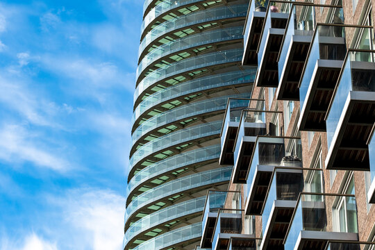 Against blue sky in London, Isle of Dogs, England, a curved residential tower shows glass balconies and a layered facade, where architecture meets open sky.