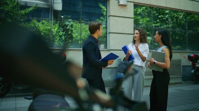 A diverse group of business colleagues engages in an outdoor meeting and discussion. They are seen collaborating and communicating on a city street.