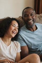 Obraz premium Happy diverse couple laughing together on a comfortable sofa at home, joy, connection, and domestic life