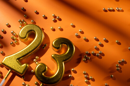 vibrant festive backdrop for 23rd birthday, made of gold candles shaped like number twenty-three, placed on an orange background with sprinkles. versatile festive banner with space for text.