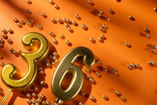 vibrant festive backdrop for 36th birthday, made of gold candles shaped like number thirty-six, placed on an orange background with sprinkles. versatile festive banner with space for text.