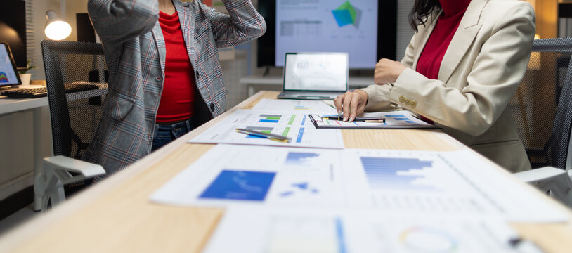 Businesswoman analyzing data charts during a late night meeting. Two businesswomen discussing financial data and graphs, working together on a project in an office during overtime.